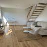 Modernes Wohnzimmer mit Holztreppe, Sofa, Sessel und Tisch.
