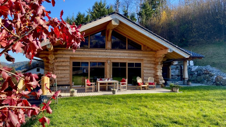 Holzchalet mit Terrasse und roten Herbstbl&auml;ttern im Vordergrund.