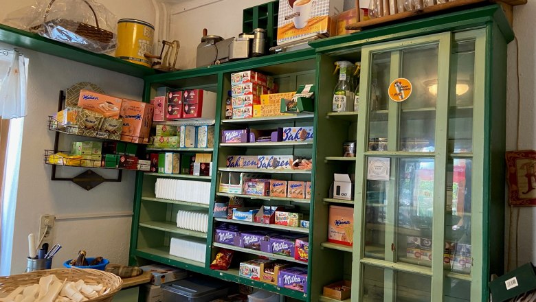 Ein traditioneller Laden mit gr&uuml;nen Regalen, gef&uuml;llt mit verschiedenen Lebensmitteln und Haushaltswaren.