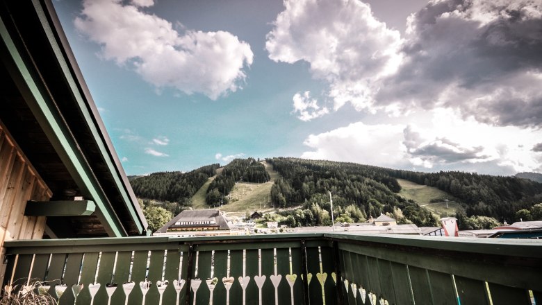 Blick von einem Balkon auf eine gr&uuml;ne Berglandschaft mit Wolken am Himmel.