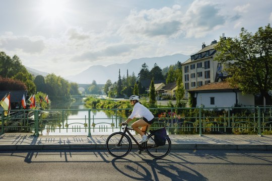 Frau auf dem Fahrrad, die über eine Brücke eines Flusses fährt