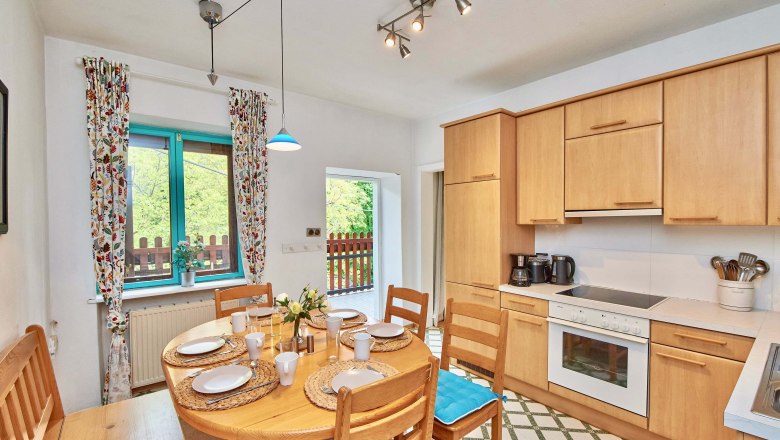 Gemütliche Küche mit Holzmöbeln, Esstisch und Fenster mit bunten Vorhängen.