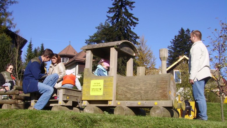 Kinder spielen auf einem hölzernen Zug im Freien.
