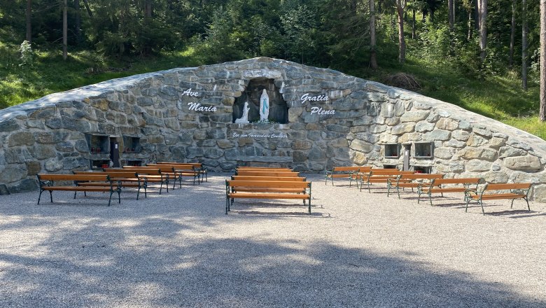 Steingrotte mit Marienstatue und Bänken davor im Freien.