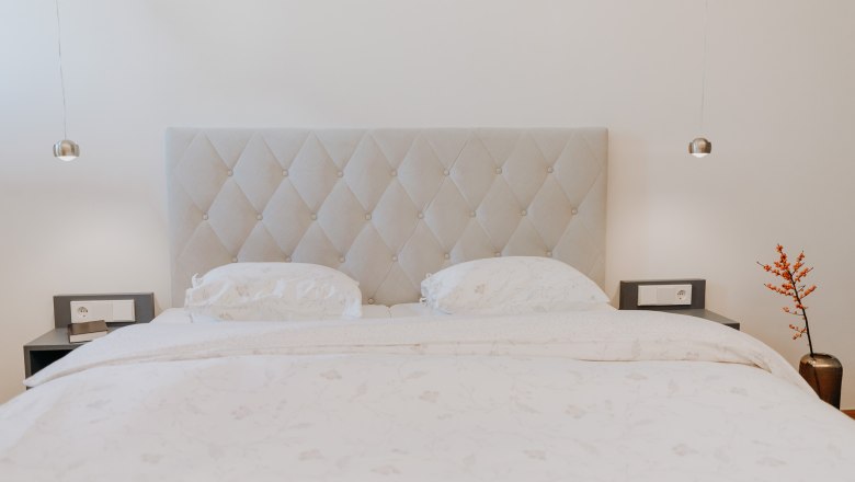 Ein elegantes Schlafzimmer mit einem großen Bett, zwei Nachttischen und einer Vase mit roten Beeren.