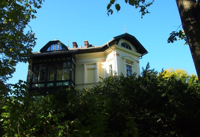 Historische Villa hinter Bäumen, blauer Himmel.