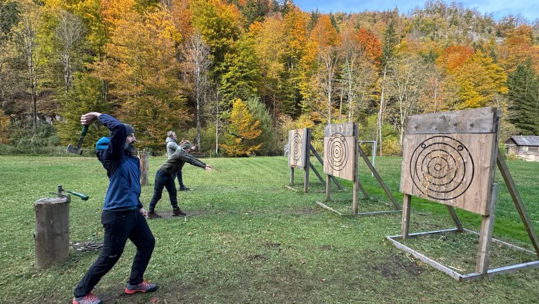 Personen werfen Äxte auf Zielscheiben im Freien, umgeben von herbstlichen Bäumen.