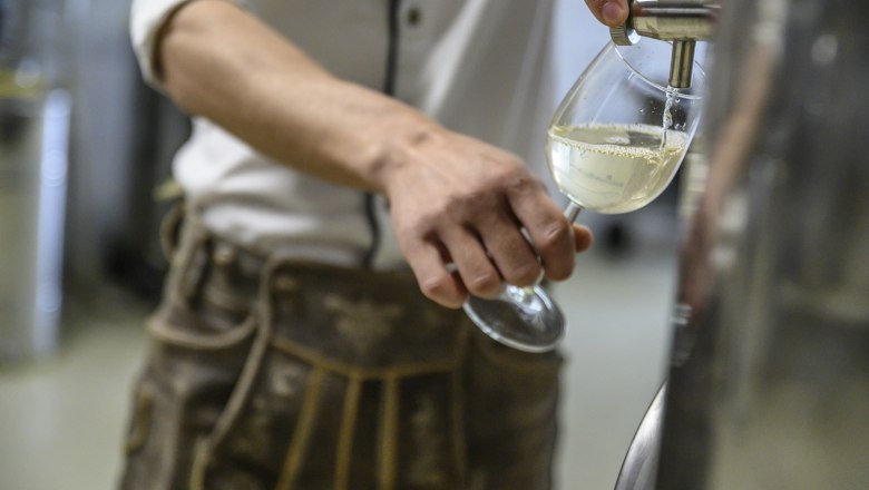 Person füllt ein Glas mit weißem Getränk aus einem Edelstahlbehälter.