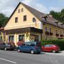 Ein gelbes Gasthaus mit roten Blumen und parkenden Autos davor.