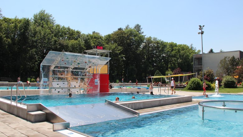 Freibad mit Kletterwand, umgeben von Bäumen.