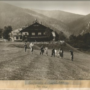 Auf dem Golfplatz stehen einige Spieler und im Hintergrund ein Geb&auml;ude, die Meierei und bewaldete H&uuml;gel.