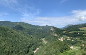Panoramablick auf eine grüne Berglandschaft mit einem kleinen Dorf und einem Viadukt.
