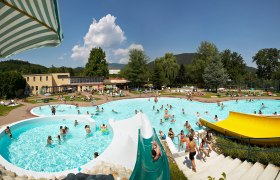 Ein Freibad mit mehreren Pools, Wasserrutschen und vielen Menschen an einem sonnigen Tag.