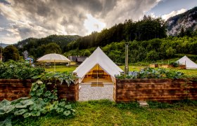 Glamping-Zelt in gr&uuml;ner Landschaft mit Bergen im Hintergrund.