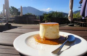 Ein Teller mit Schafkäse, Honig und Zimt auf einer Terrasse mit Bergblick.