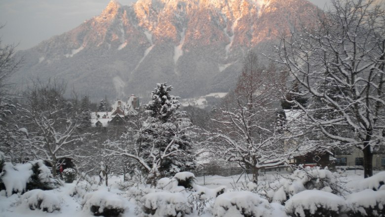 Verschneite Landschaft mit Bergen im Hintergrund, beleuchtet von der Abendsonne.