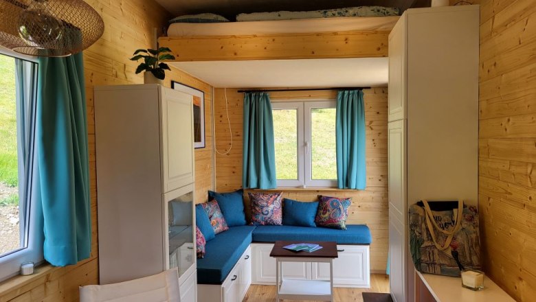 Kleiner Wohnbereich mit Hubbett, blauen Vorhängen und Holzwänden.