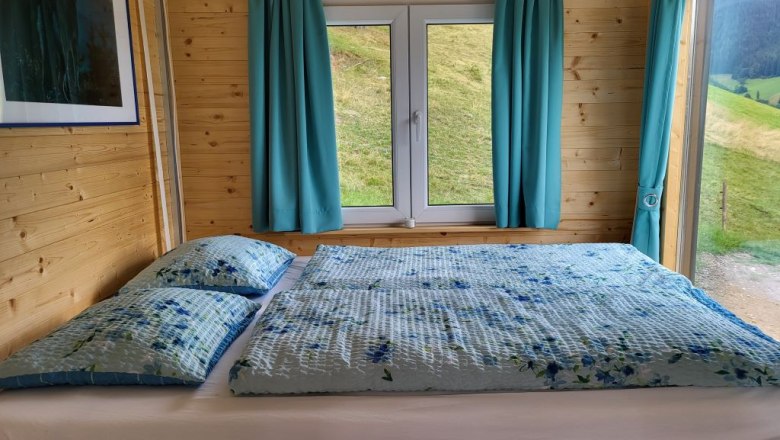 Holzinterieur mit Bett, Fenster und blauen Vorhängen.
