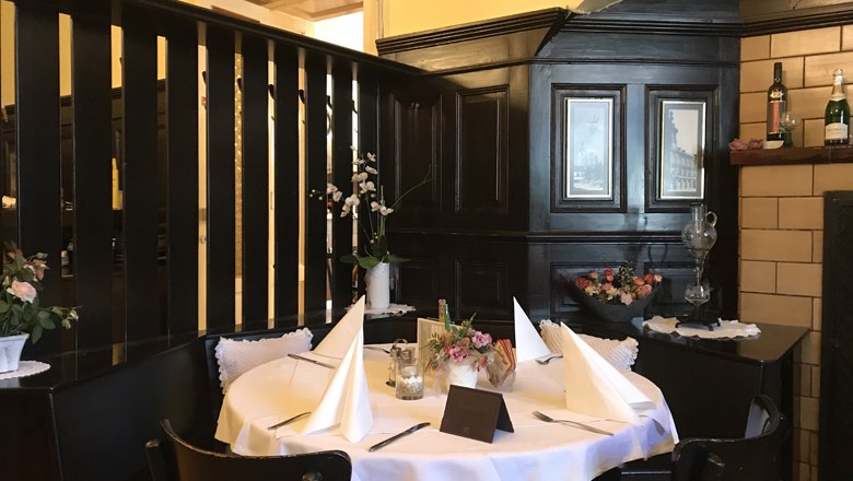 Ein gem&uuml;tlicher Tisch in einem traditionellen Restaurant mit dunkler Holzvert&auml;felung und dekorativen Blumen.