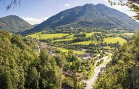 Panoramablick auf ein gr&uuml;nes Tal mit Bergen im Hintergrund und einem Dorf im Vordergrund.