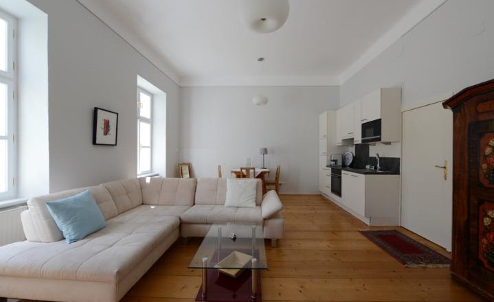 Helles Wohnzimmer mit Ecksofa, Glastisch, Esstisch und K&uuml;chenzeile.