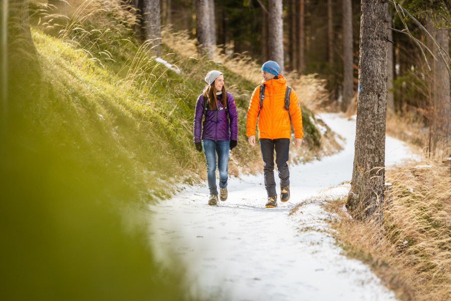 eine Frau und ein Mann in Winterkleidung wandern entlang eines leicht schneebedeckten Weges