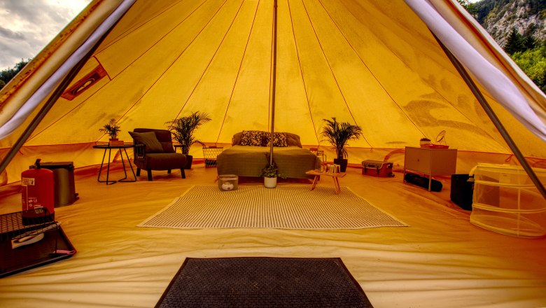 Innenansicht eines luxuri&ouml;sen Glamping-Zeltes mit Bett, Pflanzen und M&ouml;beln.