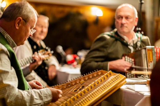 Drei Musikanten mit Zither und Steirischer Harmonika musizieren im weihnachtlichem Ambiente