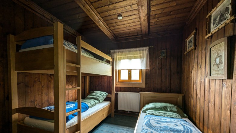 Holzvertäfeltes Dreibettzimmer mit Etagenbett und Einzelbett, Fenster mit Vorhang, rustikale Einrichtung.