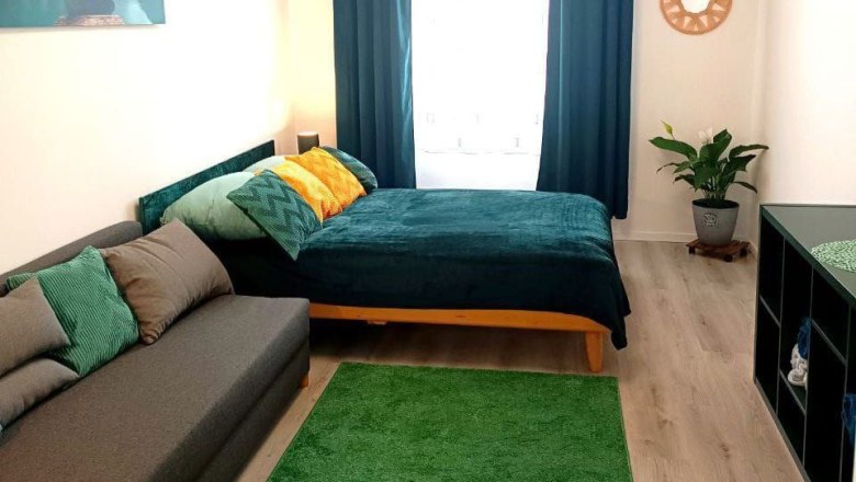 Ein gem&uuml;tlich eingerichtetes Schlafzimmer mit einem Bett, Sofa, gr&uuml;nen Teppich und Pflanzen.