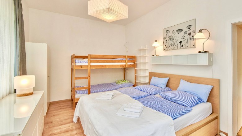 Schlafzimmer mit Doppelbett und Etagenbett, helle Einrichtung.