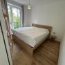Helles Schlafzimmer mit Holzboden, Doppelbett und Fenster mit Blick ins Grüne.