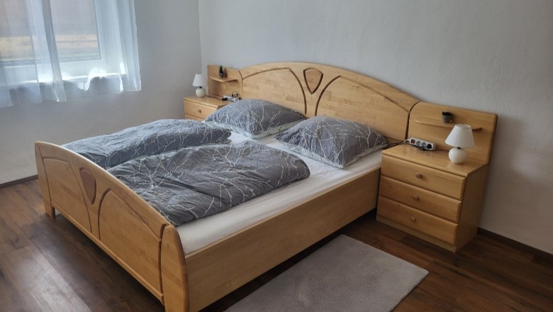 Schlafzimmer mit Doppelbett, Holzmöbeln und grauer Bettwäsche.