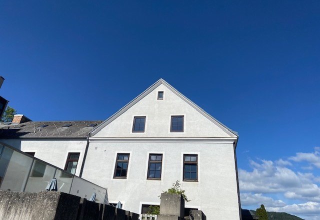 Weißes Gebäude mit Giebeldach vor blauem Himmel.