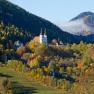 Herbstliche Landschaft mit Kirche in Maria Schutz, umgeben von bunten Bäumen und Hügeln.