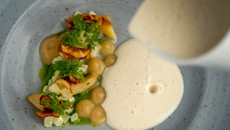 Gourmetgericht mit Schaum und Gemüse auf einem Teller.