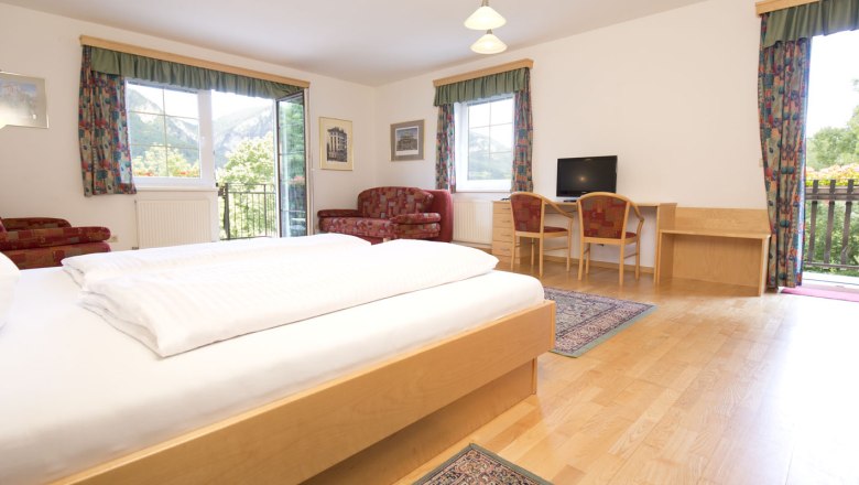 Doppelzimmer mit Holzboden und roter Couch sowie bunten Vorhängen