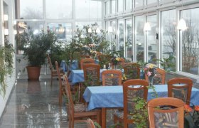 Ein Wintergarten mit Tischen, blauen Tischdecken und vielen Pflanzen.