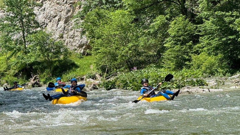 Personen beim Tubing auf einem Fluss in einer gr&uuml;nen, bewaldeten Umgebung.