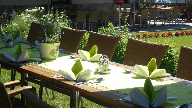 Gedeckter Tisch im Garten mit grünen Servietten und Blumen.