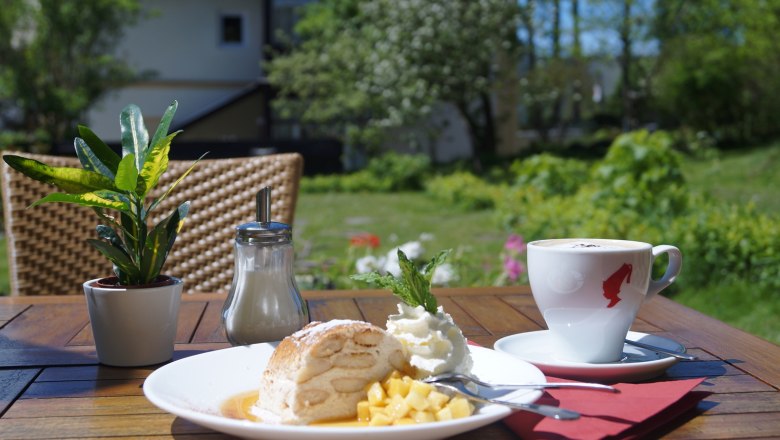 Ein Teller mit Dessert und eine Tasse Kaffee auf einem Tisch im Freien.