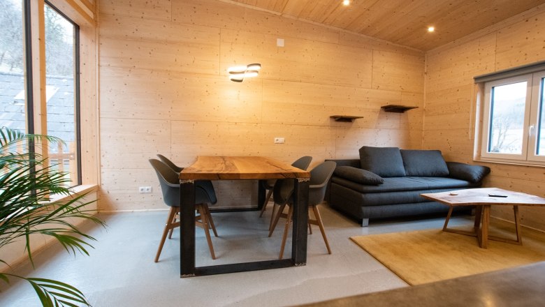 Moderner Essbereich mit Holztisch, grauen Stühlen und Sofa in einem Raum mit Holzverkleidung.