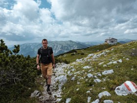 Ein Wanderer genießt die frische Bergluft und die atemberaubende Aussicht auf die umliegenden Gipfel. Die sanften Hügel und das grüne Gras laden dazu ein, die Natur in vollen Zügen zu erleben. Hier, in den Wiener Alpen, wird jeder Schritt zu einem unvergesslichen Abenteuer.